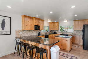 Kitchen featuring sink, light wood-type flooring, kitchen peninsula, and black appliances