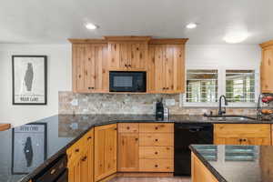 Kitchen with dark stone counters, black appliances, tasteful backsplash, sink, and light hardwood / wood-style floors