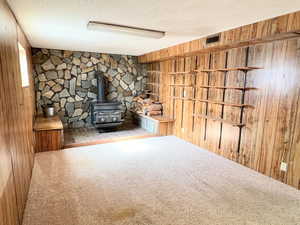 Unfurnished living room with wood walls, a wood stove, carpet flooring, and a textured ceiling