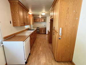 Kitchen with dishwasher, light LVP/ wood-style floors, sink, and a textured ceiling