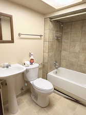 Bathroom with tile patterned linoleum flooring, tiled shower / bath combo, and toilet