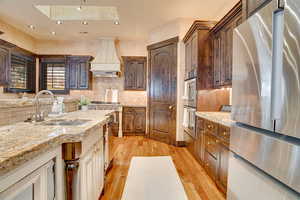 Kitchen featuring a sink, appliances with stainless steel finishes, custom exhaust hood, decorative backsplash, and wood finished floors