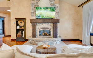 Living room with a stone fireplace, baseboards, and wood finished floors