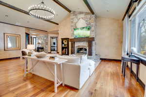 Living room featuring a notable chandelier, a stone fireplace, beam ceiling, and wood-style floors