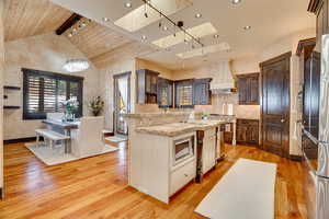 Kitchen featuring stainless steel appliances, skylights, a sink, custom exhaust hood, and wood finished floors