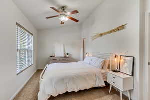 Primary bedroom with ceiling fan, vaulted ceiling, and en suite bathroom.