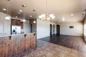 Kitchen featuring a notable chandelier, hardwood / wood-style flooring, light stone countertops, stainless steel fridge, and a kitchen breakfast bar