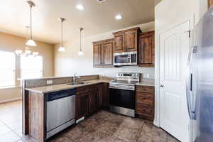 Kitchen with sink, appliances with stainless steel finishes, pendant lighting, and dark tile patterned floors