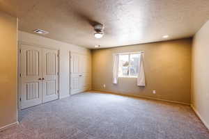 Unfurnished bedroom featuring multiple closets, carpet, a textured ceiling, and ceiling fan