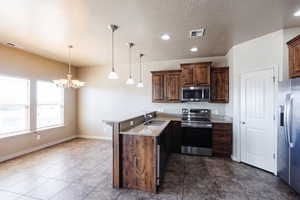 Kitchen with appliances with stainless steel finishes, sink, kitchen peninsula, pendant lighting, and dark tile patterned flooring