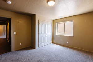 Unfurnished bedroom featuring a textured ceiling, a closet, and carpet flooring