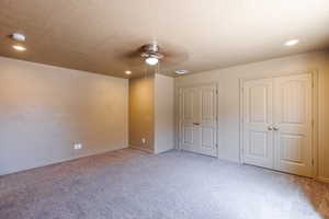 Unfurnished bedroom featuring two closets, carpet floors, a textured ceiling, and ceiling fan