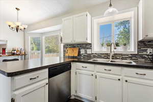 Kitchen with tasteful backsplash, white cabinets, sink, hanging light fixtures, and dishwasher