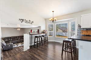 Dining space with dark hardwood / wood-style floors, vaulted ceiling, and ceiling fan with notable chandelier