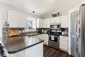 Kitchen with appliances with stainless steel finishes, vaulted ceiling, sink, kitchen peninsula, and hanging light fixtures