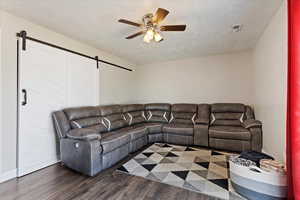 Living room featuring dark wood-type flooring, a barn door, and ceiling fan