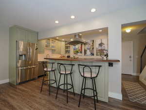 Kitchen featuring a kitchen breakfast bar, dark hardwood / wood-style floors, stainless steel fridge, extractor fan, and butcher block countertops