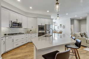 Kitchen featuring tasteful backsplash, stainless steel appliances, sink, pendant lighting, and light hardwood / wood-style floors