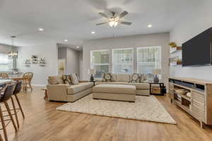 Living room featuring ceiling fan with notable chandelier and light wood-type flooring