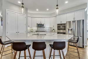 Kitchen with an island with sink, light hardwood / wood-style floors, appliances with stainless steel finishes, decorative backsplash, and sink