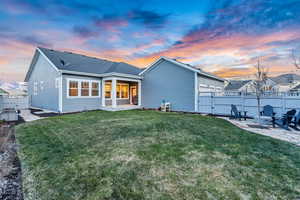 Back house at dusk featuring a yard and a patio area