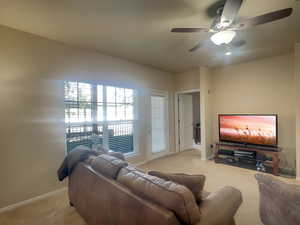 Living area with light carpet, a ceiling fan, and baseboards
