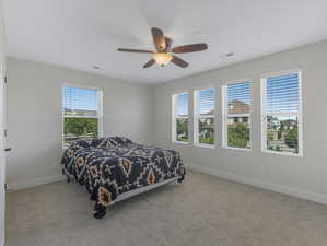 Bedroom featuring light carpet, multiple windows, and ceiling fan