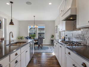 Kitchen with dark hardwood / wood-style floors, hanging light fixtures, white cabinets, and custom exhaust hood