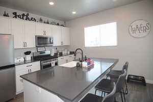 Kitchen with white cabinets, stainless steel appliances, sink, an island with sink, and dark hardwood / wood-style flooring