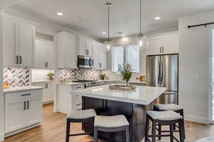 Kitchen featuring stainless steel appliances, hanging light fixtures, a center island, light hardwood / wood-style floors, and backsplash