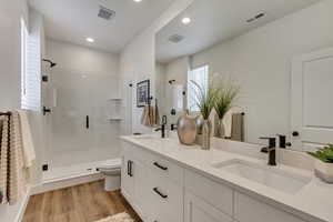 Bathroom with hardwood / wood-style flooring, a shower with shower door, toilet, and dual bowl vanity