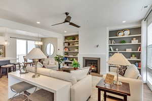 Living room featuring built in shelves, light hardwood / wood-style flooring, ceiling fan with notable chandelier, and plenty of natural light