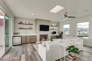 Living room with a skylight, sink, light hardwood / wood-style flooring, and ceiling fan