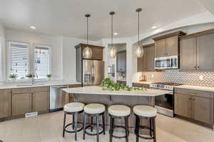 Kitchen featuring stainless steel appliances, hanging light fixtures, sink, a kitchen island, and backsplash