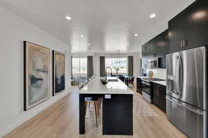 Kitchen with appliances with stainless steel finishes, sink, decorative light fixtures, light wood-type flooring, and an island with sink