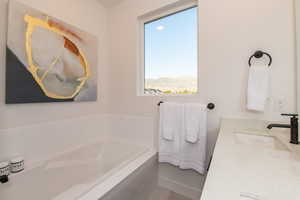 Bathroom featuring a relaxing tiled tub, vanity, and a healthy amount of sunlight