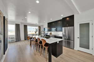 Kitchen with light hardwood / wood-style flooring, a kitchen island with sink, appliances with stainless steel finishes, pendant lighting, and a kitchen bar