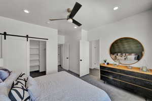 Carpeted bedroom with a closet, a barn door, ceiling fan, and a spacious closet