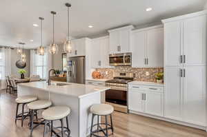 Kitchen featuring decorative light fixtures, stainless steel appliances, sink, a center island with sink, and light hardwood / wood-style floors