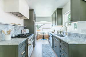 Kitchen with light hardwood / wood-style flooring, green cabinetry, sink, light stone countertops, and appliances with stainless steel finishes