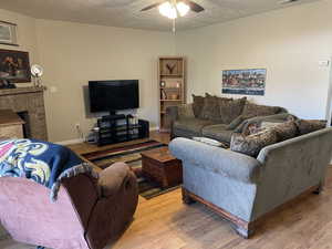 Living room with a textured ceiling, light hardwood / wood-style flooring, a brick fireplace, and ceiling fan