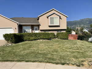 Split level home featuring a mountain view, a garage, and a front lawn