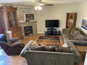 Living room featuring a fireplace, a textured ceiling, ceiling fan, and hardwood / wood-style floors