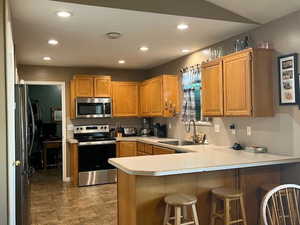 Kitchen with tile patterned floors, a kitchen bar, sink, kitchen peninsula, and stainless steel appliances