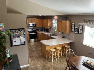 Kitchen featuring appliances with stainless steel finishes, sink, tile patterned floors, a textured ceiling, and kitchen peninsula