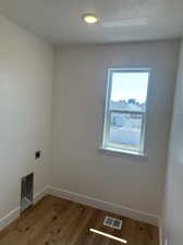 Clothes washing area featuring light hardwood / wood-style floors, hookup for an electric dryer, and a textured ceiling