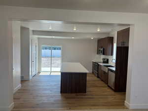 Kitchen with dark brown cabinets, tasteful backsplash, stainless steel appliances, a kitchen island, and light hardwood / wood-style flooring