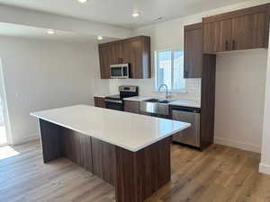 Kitchen with backsplash, a kitchen island, appliances with stainless steel finishes, and light wood-type flooring