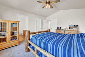 Bedroom with light carpet, ensuite bath, ceiling fan, and vaulted ceiling