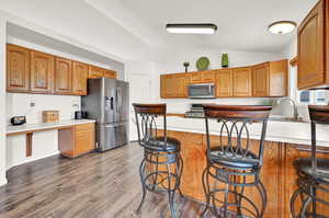 Kitchen featuring stainless steel appliances, hardwood / wood-style floors, sink, vaulted ceiling, and a breakfast bar